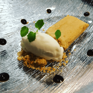 Plato dulce de helado sobre preparado de migas decorado con hierba y salsa negra.