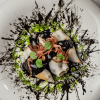 Calamares rellenos con salsa negra y verde con pulpo por encima en plato blanco. Tenedor y cuchillo.